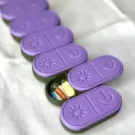 urple pill organizer with open compartments displaying pills and supplements inside, designed for daily medication management.