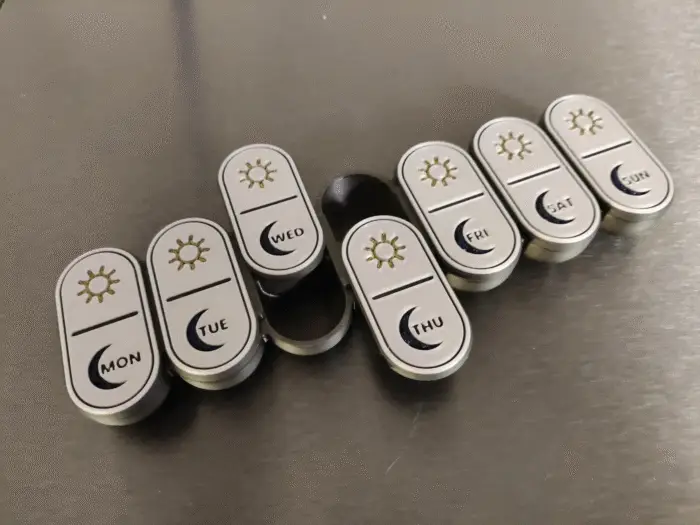 Black and white 3D-printed pill organizers with engraved sun and moon symbols, offering a stylish alternative color option