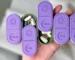 3D-printed weekly AM/PM pill organizer in purple and green, with sliding lids for easy access, held in hand for size reference.